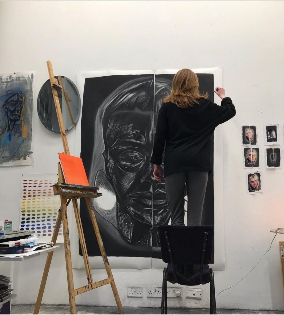 Artist Aine Rose standing on a chair and working on one of her art pieces